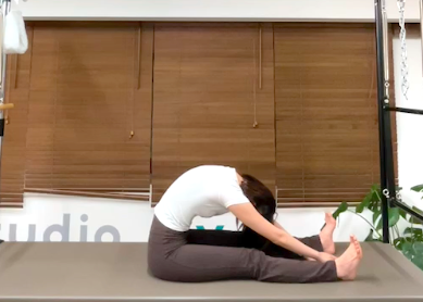 ピラティスの「スパイン・ストレッチ」を行う女性